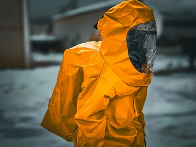 Worker in an orange hooded protective suit with a dark visor outdoors
